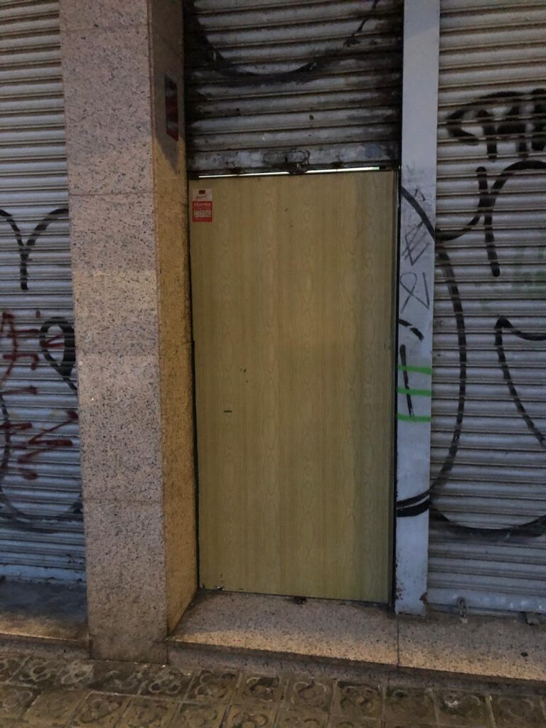 Puerta antiokupa instalada en acceso a local urbano con persiana metálica y grafitis
