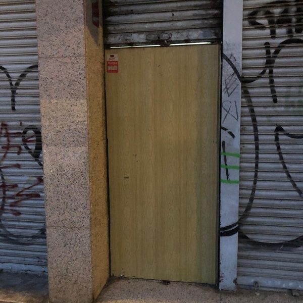 Puerta antiokupa instalada en acceso a local urbano con persiana metálica y grafitis